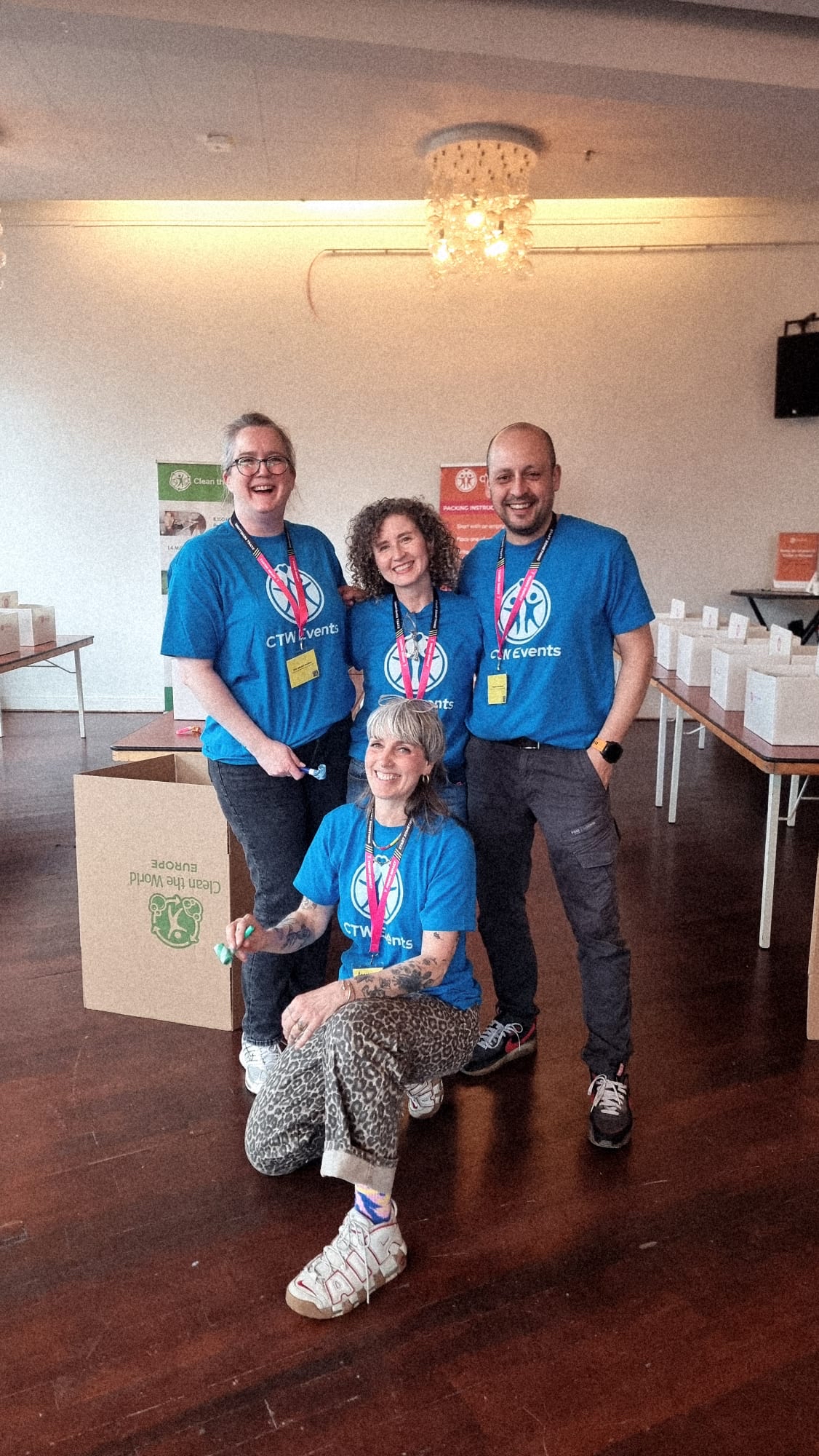 Four members of the CTW Events team in blue CTW Events T-shirts in the kit-building room before the session, with build tables behind them